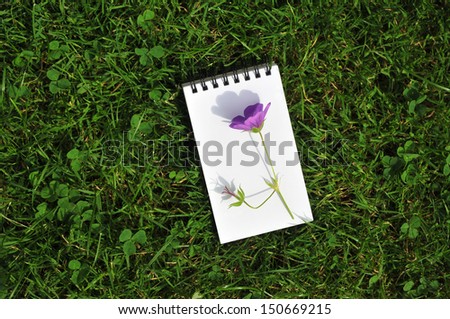 blank notepad with violet flower on grass field
