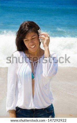 Beautiful latin (hispanic) woman hearing the sounds of seashell by the ocean