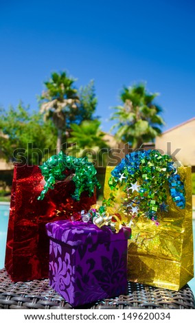 red and gold Gift bags and purple gift box with ribbon by the swimming pool with palm trees on background