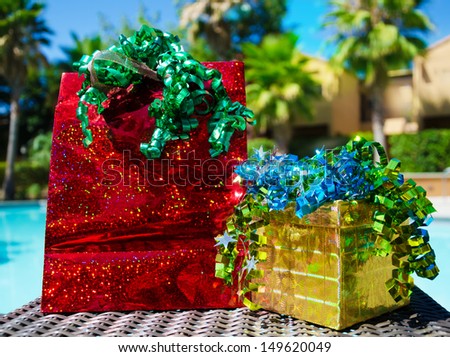 Red Gift bag and gold gift box with ribbon by the swimming pool and palm trees background