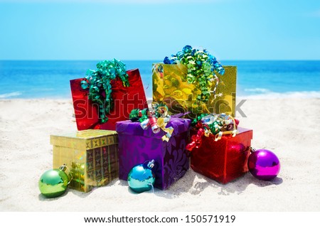 Three gift boxes and two gift bags with christmas balls on sandy beach in sunny day- holiday concept
