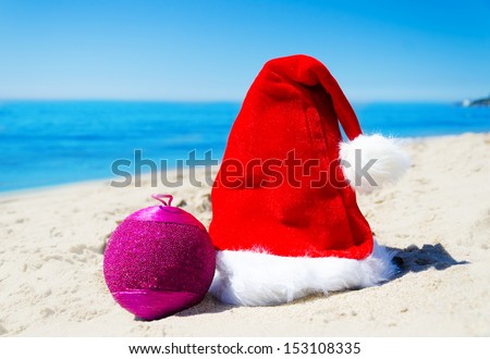 Christmas hat with christmas ball on the beach by the ocean - holiday concept