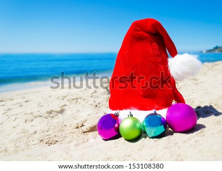 Christmas hat with christmas balls on the beach by the ocean - holiday concept