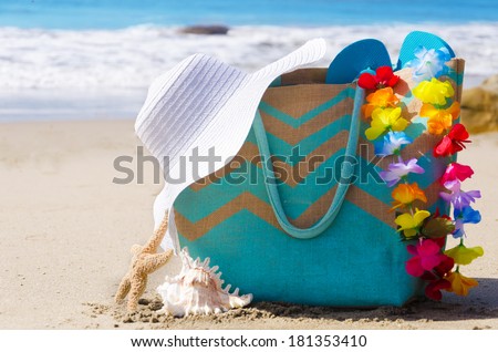 Beach bag with flip flops, decoration and woman\'s white hat by the ocean