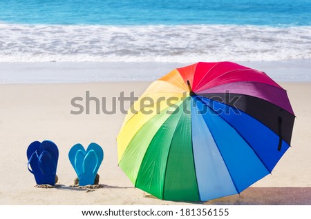 Summer background with rainbow umbrella and flip flops on the sandy beach