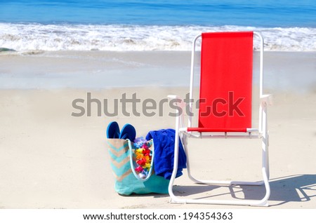 Beach chair and bag with flip flops and towel by the ocean