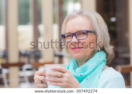 An elderly woman holding coffee cup while listening to someone at a cafe