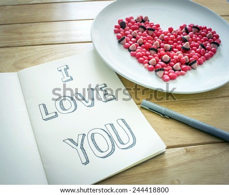 Hand drawn the sentence I LOVE YOU on notebook with sweets put in heart shape
