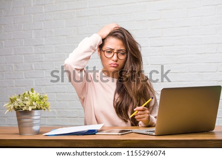 Portrait of young student latin woman sitting on her desk worried and overwhelmed, forgetful, realize something, expression of shock at having made a mistake