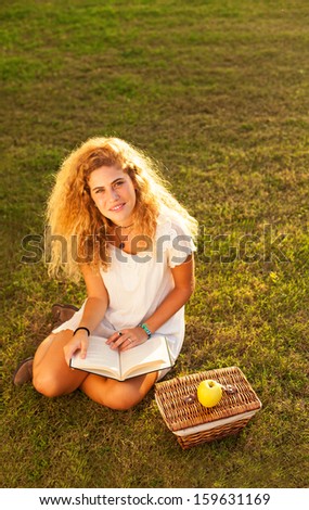 pretty blond young woman reading a book at park
