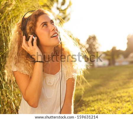 young woman listening to music at park on sunny day