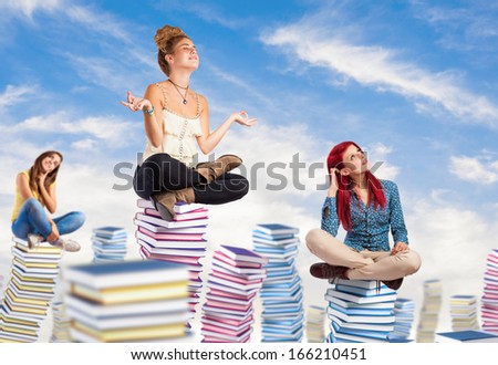 young students sitting on a big books pile on the sky