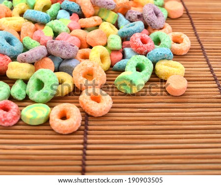 Delicious and nutritious fruit cereal loops flavorful on white background, healthy and funny addition to kids breakfast on bamboo mat