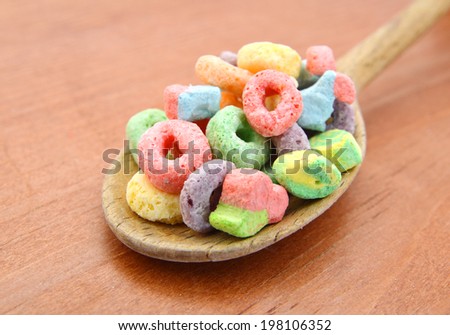 Delicious and nutritious fruit cereal loops flavorful in wooden spoon on wooden board, healthy and funny addition to kids breakfast