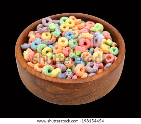 Delicious and nutritious fruit cereal loops flavorful in wooden bowl on black background, healthy and funny addition to kids breakfast