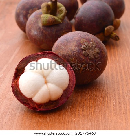 Mangosteen fruit and cross section showing the thick purple skin and white flesh of the queen of fruits on wooden board