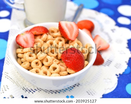White bowl full of honey corn flakes rings and strawberry - breakfast on blue background