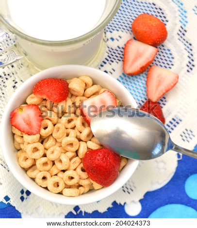 White bowl full of honey corn flakes rings and strawberry - breakfast on blue background