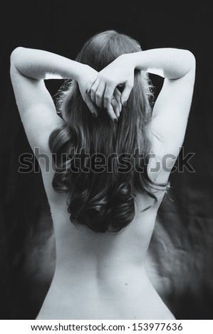 A black and white vintage styled photograph of a young woman's naked back, her hands behind her head