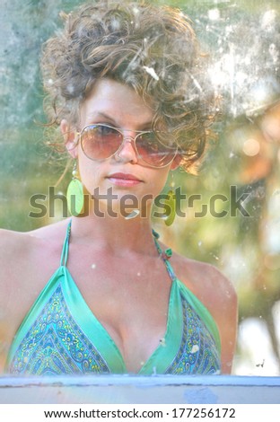 Attractive, sultry woman with curly hair, in her sunglasses and bright dress getting out of a car on a sunny day.