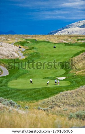 The rolling hills of a beautiful golf course and the green fairways with golfers in action in the sun with dark clouds in the background