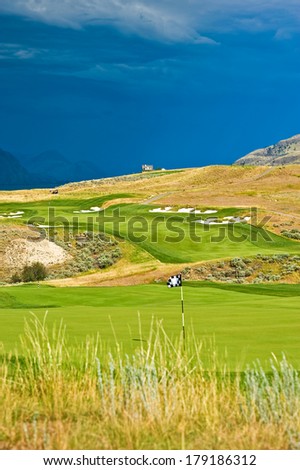 The rolling hills of a beautiful golf course and the green fairways in the sun with dark clouds in the background