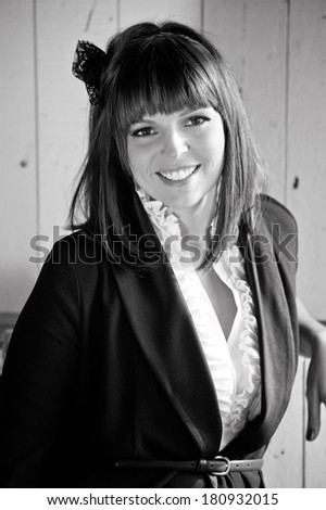 A black and white photo of an attractive woman smiling wearing formal horse riding clothes next to an old door