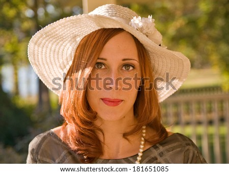 Portrait of a young woman in the sun wearing a forties dress, pearls and a big floppy white sun hat