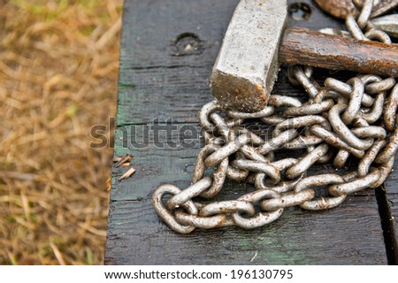 A sledge hammer and chain sitting on a wooden block in the rain