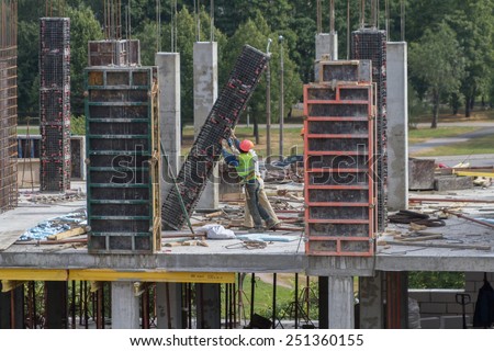 Two workers of the builder in helmets push a plate on building of the new house