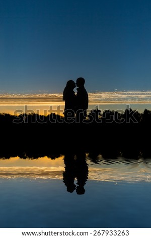 Two young people (the guy and the girl) kiss on a sunset. Romantic kiss outdoors on a sunset. romantic. Reflection in water of couple of lovers who kiss and embrace outdoors on a sunset.