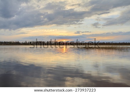 Sunset on the lake in the spring. A fiery colourful clear fine sunset in the spring on the lake with reflection of clouds in water