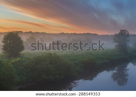 Foggy morning in the village at the river. Sunrise on the river bank in the village. Bright fine sunrise. Dawn bright clouds over the village at the river. Early twilight outdoors. Sunrise in Russia