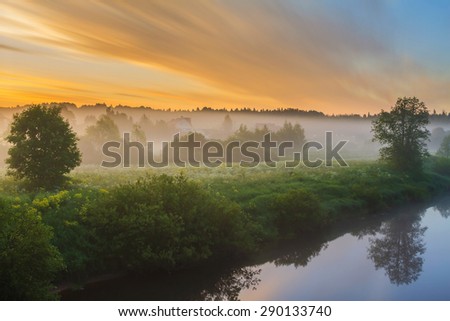 Dawn bright clouds over the village at the river. Early twilight outdoors. Sunrise in Russia. Foggy morning in the village at the river. Sunrise on the river bank in the village. Bright fine sunrise.
