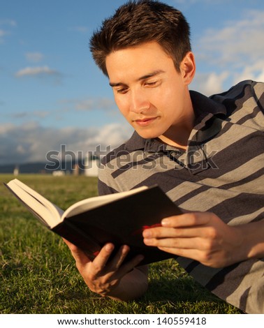 Handsome young man reading a book at the park