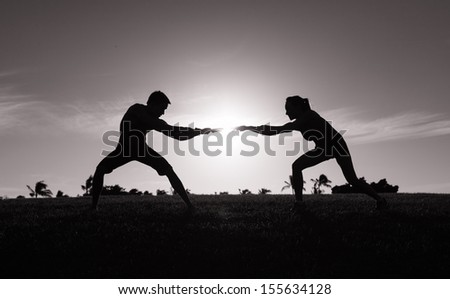 Silhouette male and female playing tug of war