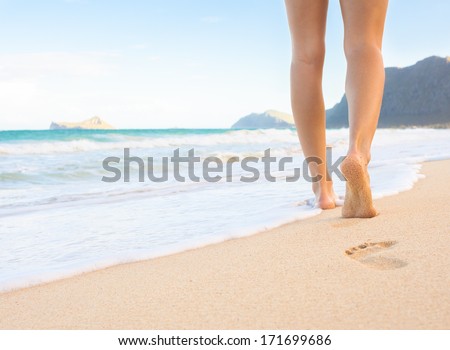 Woman walking on sand beach leaving footprints in the sand. Beach travel.
