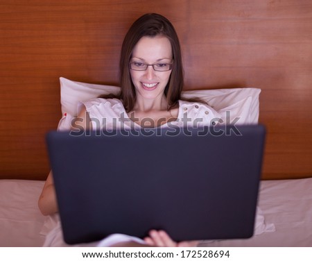 Portrait of pretty woman lying in the bed with a laptop smiling
