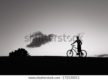 Silhouette of young athlete with bicycle at sunset