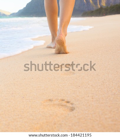 Beach travel - beautiful girl walking on sand beach leaving footprints in the sand. Closeup detail of female feet and golden sand on beach in Hawaii.
