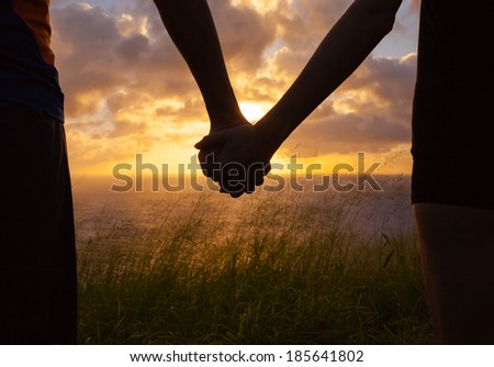 Couple holding hands a watching a beautiful sunset in Hawaii.