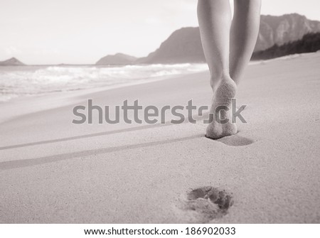 Beach travel - woman walking on sand beach leaving footprints in the sand. Close up detail of female feet and sand on beach in Hawaii, USA.