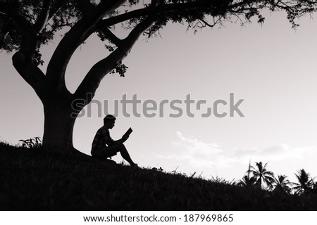 Silhouette of boy reading book in the park.