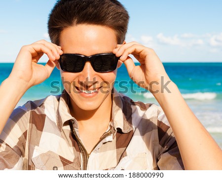 Happy smiling man on the beach. Young male model enjoying summer travel holiday by the ocean.