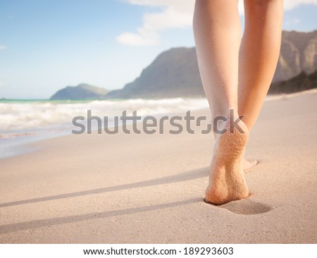 Woman walking on sand beach leaving footprints in the sand. Closeup of female feet at the beach in Hawaii. Beach travel.