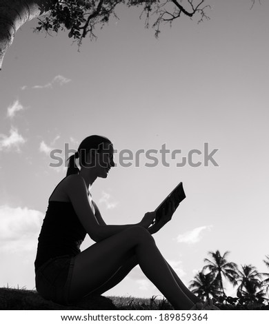 Woman sitting down in a garden and reading a book. Education concept.