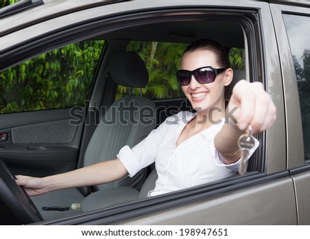 Happy woman driver showing car keys from the window. New car, rental or driving rental concept.