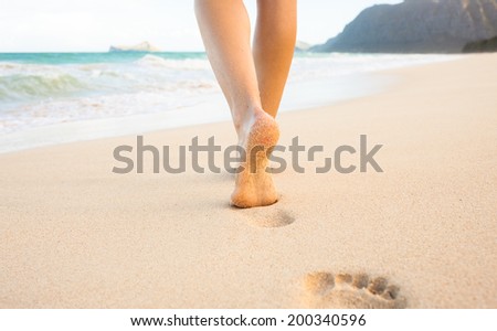 Beach travel - woman walking on sand beach leaving footprints in the sand. Closeup detail of female feet and golden sand on Maui, Hawaii, USA.