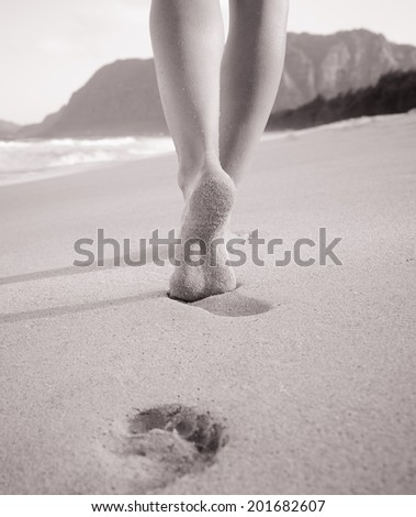 Woman walking on sand beach leaving foot prints in the sand - beach travel concept.