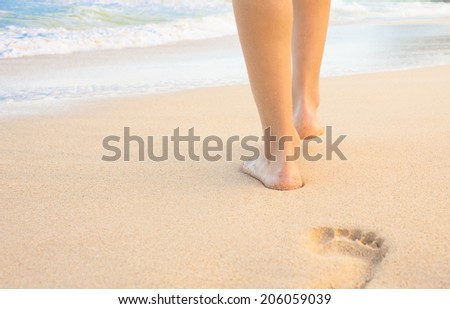 Beach travel - Close up of a woman walking on sandy beach leaving footprints in the sand.